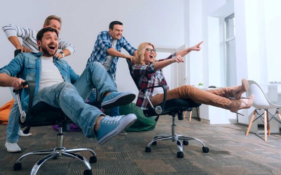 Happy employees playing around using office chairs.